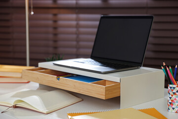 Fototapeta premium Workplace with laptop on riser stand and stationery indoors, closeup