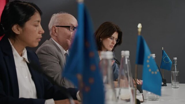 Senior man speaking at international summit panel with diverse colleagues listening. Ideal for news broadcasts, political campaigns, and corporate communication videos side view shot