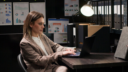 Confident female private detective investigator reviews clues in office, searching on laptop for evidence to solve crime, profile portrait of focused Caucasian policewoman using personal computer. © DC Studio