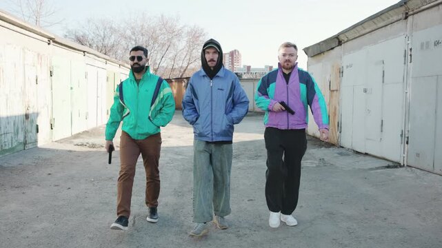 Three Men In Retro Outerwear Stroll Along Urban Industrial Alley Under Cold Sunlight Casting Long Shadows . Media
