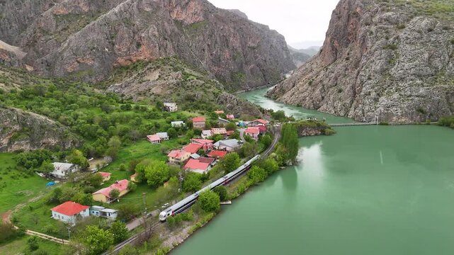 Aerial view of a passenger train traveling through a scenic canyon along a turquoise river.