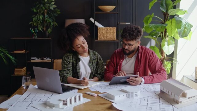 Diverse architects discuss house model and plans at studio desk