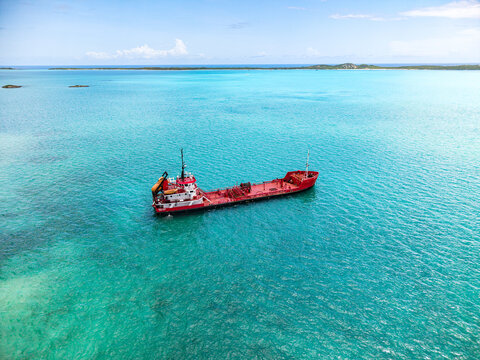 Aerial view of a red cargo ship anchored in the turquoise tropical waters near the coastline under a clear blue sky George Town, Exuma, The Bahamas.