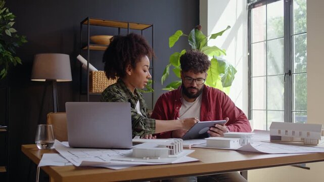 Architects review tablet and house model at sunlit studio desk