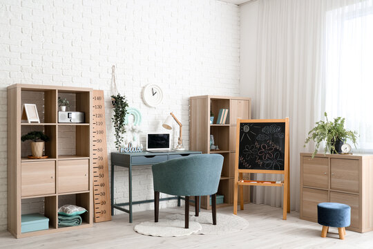 Modern childrens room interior with comfortable workspace, laptop and wooden stadiometer