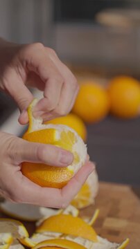 Hands peel orange over cutting board with orange peel pieces around. Concept of citrus recipe preparation and homemade candied peel