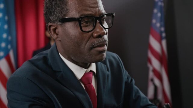 Black man as politician speaking passionately and gesturing with raised fist at press conference with American flags in background. Footage is ideal for political campaign videos, close up shot