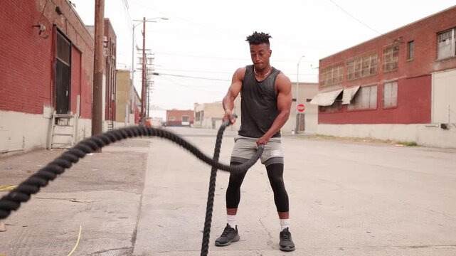 Athletic African American man with a disabled left hand working out with a battle rope in a warehouse area near downtown Los Angeles.