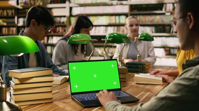 Green screen chroma key on laptop in front of study group at library table with students, green lamps framing screen replacement on desk, Editable replaceable screen, with group study and coursework.