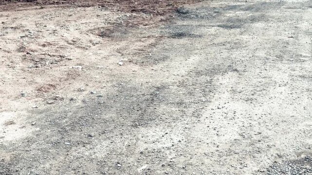Gravel road pothole damage daytime closeup of rutted asphalt and scattered rubble showing cracked surface texture, uneven patches.