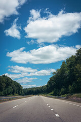 Fototapeta premium White cloudscape in the blue sky over the forest along the I‑95 Interstate highway in New England in summer