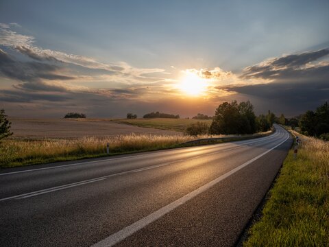 Empty asphalt road winding through idyllic rural landscape during mystical sunset