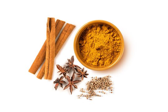 Top-down view of various whole and ground spices including  cinnamon sticks, star anise, coriander seeds, and  golden bowl of curry powder, isolated on white background. Perfect for aromatic recipes.