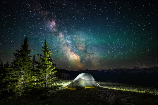 A clear, starry night with the Milky Way in the background, next to a camping tent and the rocky Canadian mountains 