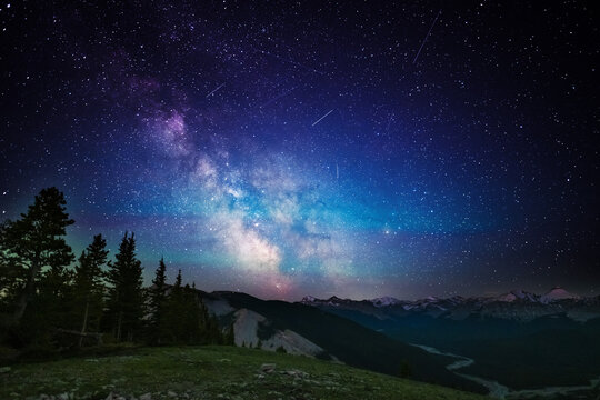 A clear, starry night with the Milky Way in the background, next to a camping tent and the rocky Canadian mountains 