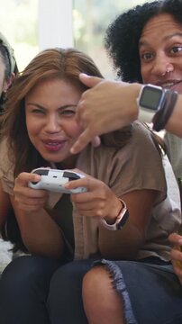 Vertical video: Laughing woman holding gamepad at start, pulling to keep from pal with beer at home