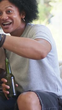 Vertical video: Laughing man in gray T at home holding green bottle seeing and reaching for gamepad