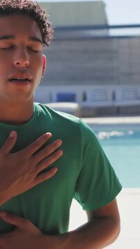 Vertical video: Breathing man starting hands on chest and belly at pool wearing green tee for calm