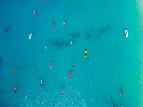 Aerial view of colorful fishing boats floating on the calm turquoise surface of the Atlantic Ocean in Santa Maria, Sal, Cabo Verde.