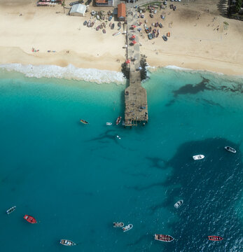 Aerial view of the Santa Maria pier and sandy beach with colorful fishing boats in the turquoise ocean Santa Maria, Sal, Cabo Verde.
