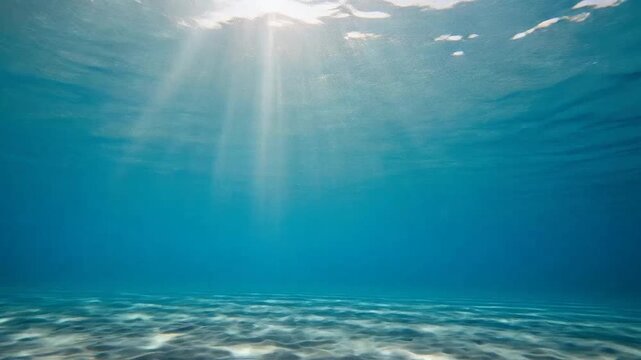 Sunlight beams through clear blue water onto a sandy ocean floor