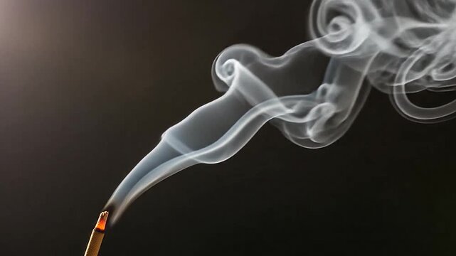 A single incense stick burning with wisps of white smoke against a dark background