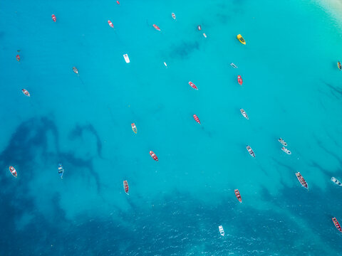 Aerial view of colorful fishing boats floating on the crystal clear turquoise waters of the Atlantic Ocean in Santa Maria, Sal, Cabo Verde.