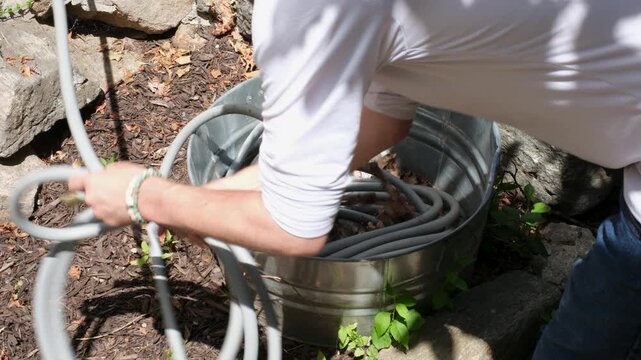 Hands unpacking a gray garden hose from a galvanized metal tub