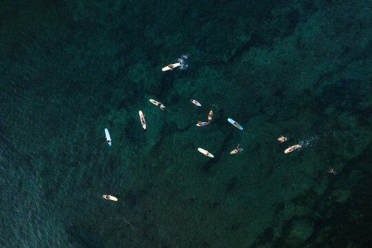 Aerial view of surfers on colorful boards floating in the clear turquoise waters of Siargao Island near General Luna, Caraga, Philippines.