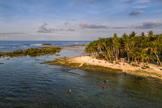 Aerial view of Siargao Island with palm trees lining the sandy beach and a wooden boardwalk extending over the clear water in General Luna, Caraga, Philippines.