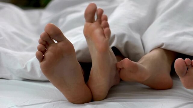 Woman touching husband leg in bed, flirt and intimacy relations sensually romantic, close-up.