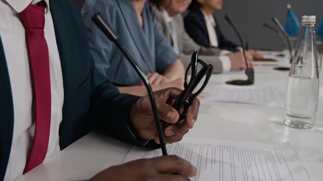 Black adult politician holding glasses and sitting at conference table during international summit. Clip is ideal for projects on global diplomacy and corporate governance close up shot