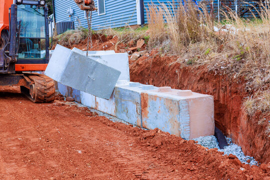 Construction work takes place site with excavator lifts placing blocks on prepared retaining walls