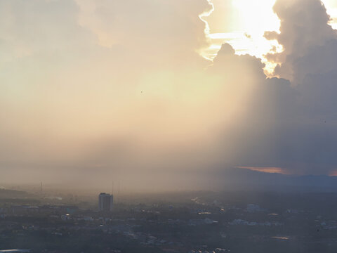 Industrial smog or burning waste pollutants drift into the air, affecting the atmosphere and the sun. Buildings and trees obstruct the view, reducing visibility.