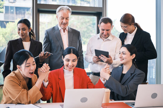 Young female CEO and multiracial partner team happy and cheerful with company incomes and stock trading investment results, watching on laptop, business success and profits, online conference meeting.