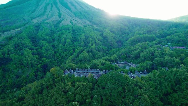 Aerial view of Bena Traditional Village with thatched roof houses nestled in lush green forest at the foot of a mountain in Kecamatan Jerebuu, Nusa Tenggara Timur, Indonesia.