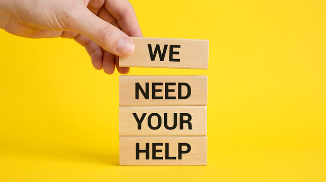 Hand holding wooden blocks with 'we need your help' on yellow background