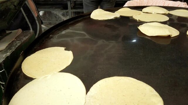 Traditional corn tortillas cooking on large hot griddle at Mexican food stall with street food preparation and handmade culinary process