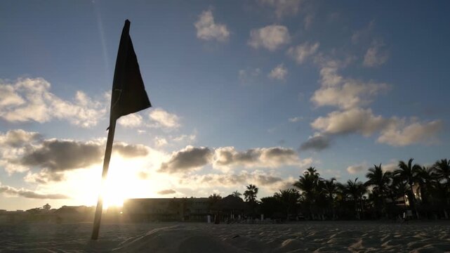 Beach warning flag near tropical shoreline with sunset sunlight palm trees dramatic clouds and peaceful coastal atmosphere during evening in Mexico