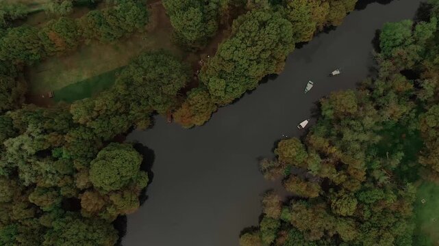 Camecuaro Lake surrounded by ahuehuete trees and calm waterways with several small boats visible near the shoreline in Zamora de Hidalgo, Michoac&aacute;n, Mexico. Descending aerial top down shot