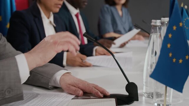 Multiethnic politicians sitting at conference table with European Union flag, reviewing documents. Perfect for international relations and global policy content side view, close up, copy space
