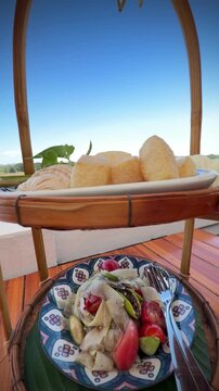Close-up of authentic Thai spicy papaya salad or call Somtum and crispy pork cracklings platter set on wooden table by river