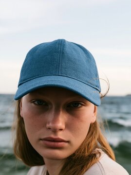 Teen girl wearing a blue baseball cap by the sea with a soft overcast sky and textured waves for a summer fashion mockup