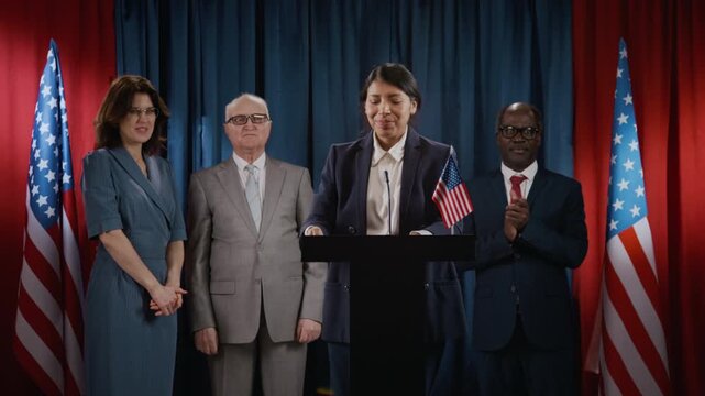 Young Hispanic female politician recording video on smartphone at podium while diverse colleagues applaud. Clip is perfect for political campaigns, news reports, and government communications