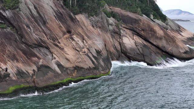 Aerial view of steep rocky cliffs and waves crashing against the shore at Praia do Leme in Rio de Janeiro, Rio de Janeiro, Brazil.