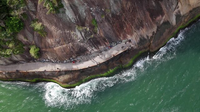 Aerial view of waves crashing against the rocky shore and the Caminho do Pescador walkway at Praia do Leme in Rio de Janeiro, State of Rio de Janeiro, Brazil.