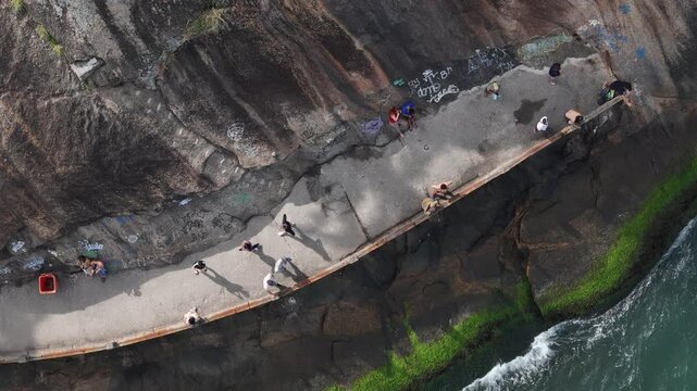 Aerial view of people walking along the coastal path at Praia do Leme with rocky cliffs and ocean waves in Rio de Janeiro, State of Rio de Janeiro, Brazil.