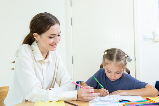 Teacher assisting young student with drawing and learning activity in classroom. Creative education, child development, personalized learning, and academic support concept.