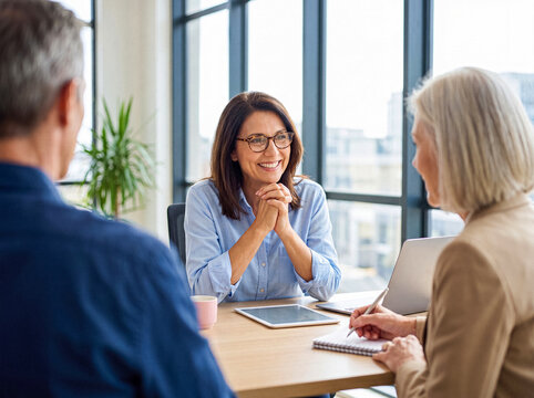 Mature financial advisor discusses future investment plans with senior couple in a modern office setting.