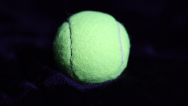 Una toma de cerca de una pelota de Tenis  con unas luces en un fondo negro